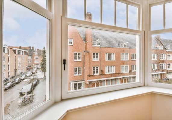Bright interior bay window with white frames overlooking a residential city street and brick buildings, filling the room with natural light and showcasing professional Window Replacement Atlanta services for enhanced comfort and energy efficiency.