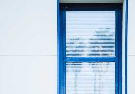 Minimalist building exterior with a blue-framed window featuring closed blinds, showcasing clean modern architecture, privacy, and professional Window Replacement Atlanta services for durability and energy efficiency.