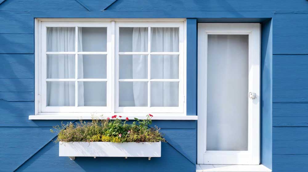 Blue home exterior with white-framed casement windows and a window flower box, featuring charming curb appeal, classic design, and professionally installed Casement Windows Atlanta for ventilation and energy efficiency.
