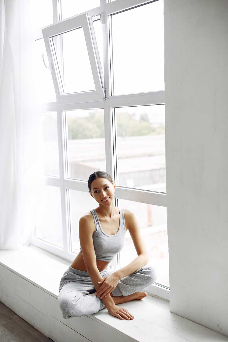 Woman sitting by an open white double hung window in a bright, airy room, enjoying fresh air and natural light, highlighting comfort, ventilation, and professionally installed Double Hung Windows Atlanta.