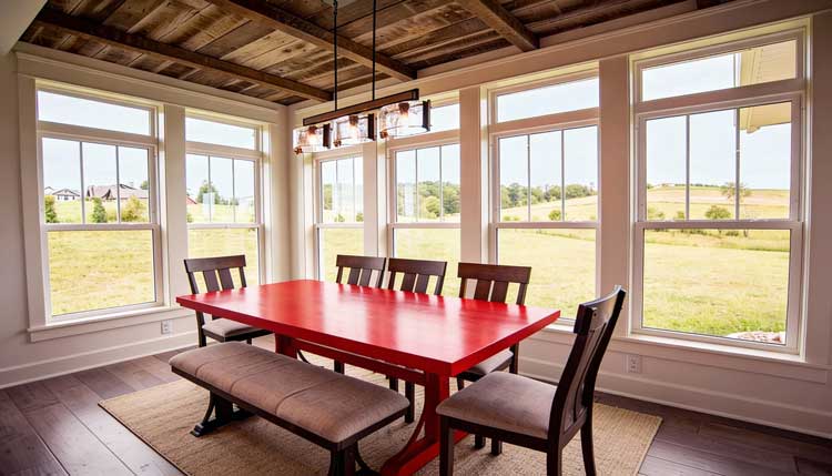 Bright dining room with a red table and multiple white-framed double hung windows overlooking open green fields, enhancing natural light, scenic views, and showcasing professionally installed Double Hung Windows Atlanta for comfort and style.