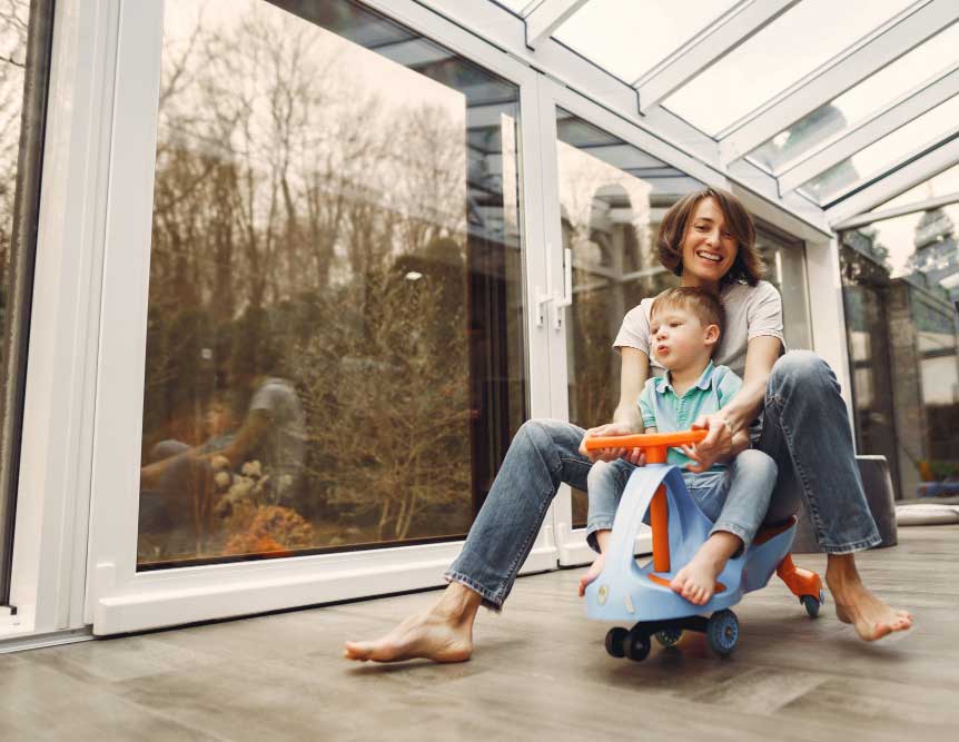 Mother and young child playing indoors beside large floor-to-ceiling windows in a bright sunroom, enjoying natural light and safety, while showcasing comfort and professional Window Replacement Marietta services for family-friendly homes.