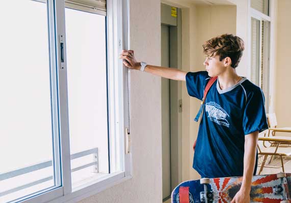 Teen standing by an open white-framed window holding a skateboard, enjoying fresh air and natural light in a modern interior, showcasing comfort and professional Window Replacement Marietta services for energy-efficient homes.