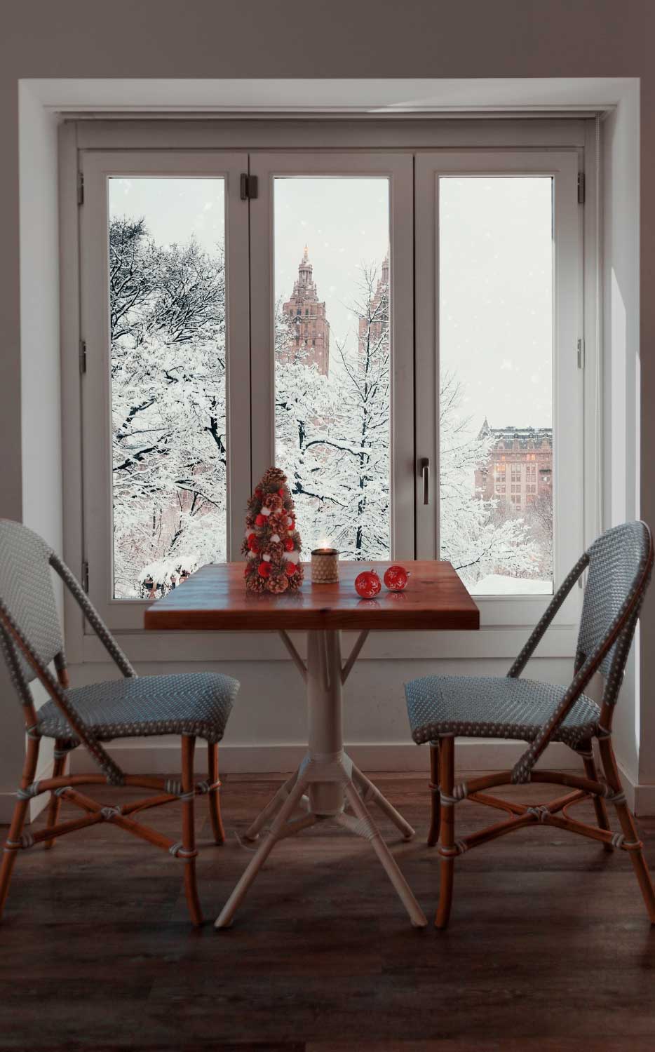 Cozy dining nook with a small table and chairs placed in front of large picture windows overlooking a snowy winter cityscape, creating a warm atmosphere while showcasing expansive views and professionally installed Picture Windows Atlanta.