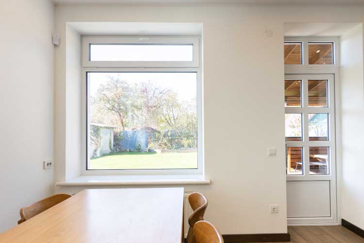 Bright dining area with a large white-framed sliding window and glass door bringing in natural light and garden views, showcasing clean modern interior design and professionally installed Sliding Windows Atlanta for comfort and energy efficiency.