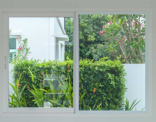 Clean interior view of a white-framed sliding window overlooking a lush green garden and landscaping, allowing natural light and outdoor views while highlighting modern design and professionally installed New & Replacement Windows Atlanta.